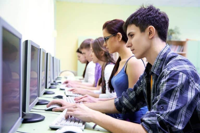 Students sitting in a row, working on computers in a classroom setting.